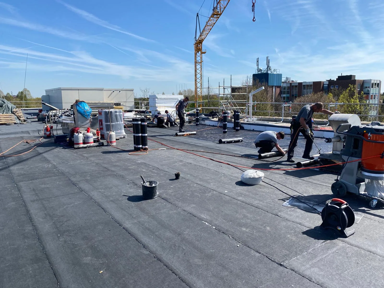 Mehrere Mitarbeiter von Hamacher Bedachungen bei der parallelen Flachdachabdichtung auf einer Betonfläche Mehrere Mitarbeiter von Hamacher Bedachungen bei der parallelen Flachdachabdichtung auf einer Betonfläche